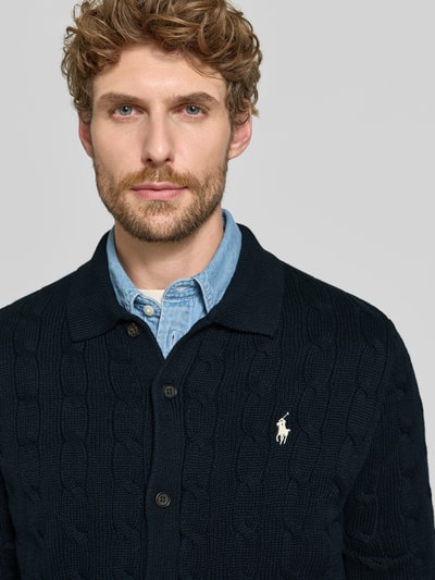 Männermodel trägt Regular Fit Strickjacke aus reiner Baumwolle von Polo Ralph Lauren in Dunkelblau, sichtbare Struktur, Nahaufnahme Oberkörper. Herren Poloshirt von Polo Ralph Lauren.