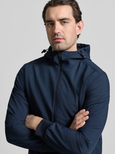 Männermodel trägt Regular Fit Funktionsjacke mit Kapuze von Tom Tailor Denim in Dunkelblau, unifarben, Nahaufnahme Oberkörper. Jacke ist wasserdicht, atmungsaktiv und wärmeisoliert, mit Stehkragen, Tunnelzug und Reißverschluss.