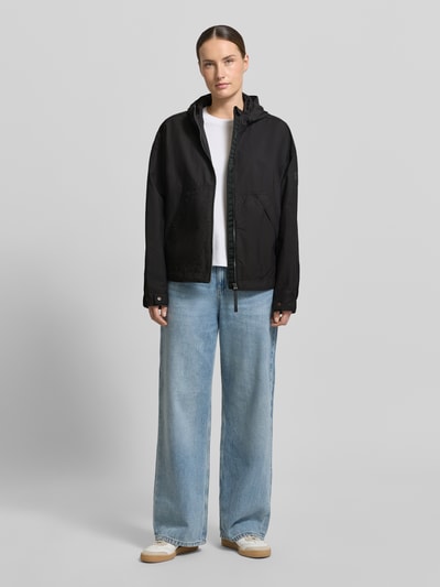 Kobieta modelka nosi kurtkę 'Jacke mit Kapuze und Zweiwege-Reißverschluss' od camel active, prosty krój, kaptur z ściągaczami, zamek błyskawiczny dwustronny, wpuszczane kieszenie, regulowane zakończenia rękawów, długość tyłu w rozmiarze 36: 67 cm, szerokość ramion: 44 cm, szerokość klatki piersiowej: 63 cm, długość rękawów: 62 cm, kolor czarny, gładka faktura, całkowity widok z przodu.