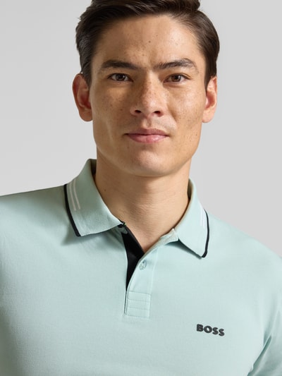 Männermodel trägt Slim Fit Poloshirt aus reiner Baumwolle Modell 'PAUL' von BOSS Green in Hellgrün, Nahaufnahme Oberkörper.