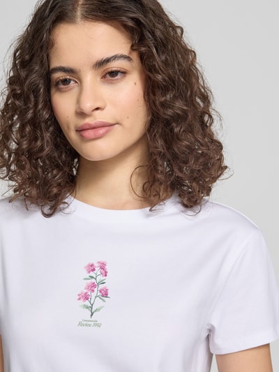 Frauenmodel trägt Schmal geschnittenes T-Shirt aus Baumwollmix mit Blumen-Print von REVIEW, weißer Stoff, rosafarbener Print, Nahaufnahme Oberkörper.