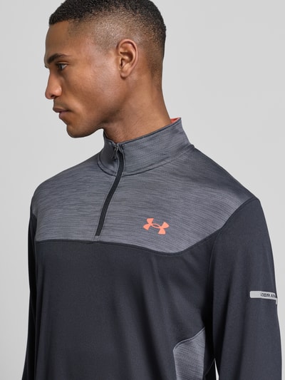 Männermodel trägt Funktionsshirt mit Stehkragen Modell 'Tech Utility 1/4 Zip' von Under Armour, Regular-Fit, Logo, Reißverschluss, Nahaufnahme Oberkörper. Rückenlänge bei Größe M: 74 cm, Ärmellänge bei Größe M: 71 cm, dunkle Farben, glatte und strukturierte Texturen.