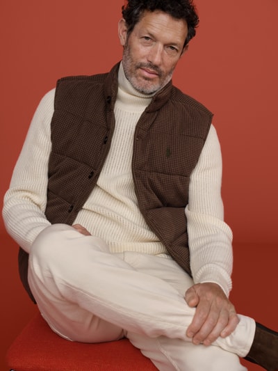 Männermodel trägt Regular Fit Weste aus reiner Baumwolle von Polo Ralph Lauren in Braun vor rotem Hintergrund, Nahaufnahme Oberkörper.