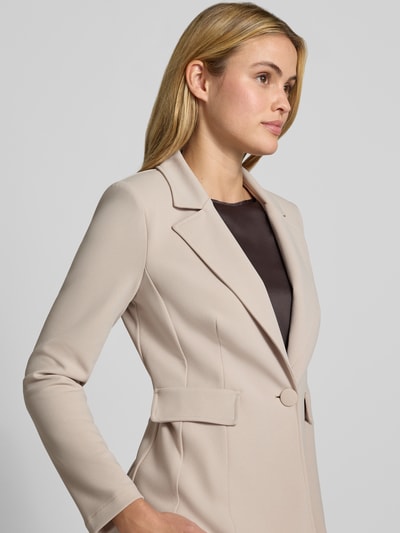 Vrouwenmodel draagt Blazer mit Reverskragen van Rinascimento in beige, elastische materiaalmix, getailleerde pasvorm, knoopsluiting, klepzakken, ruglengte bij maat S 63 cm, detailopname bovenlichaam.