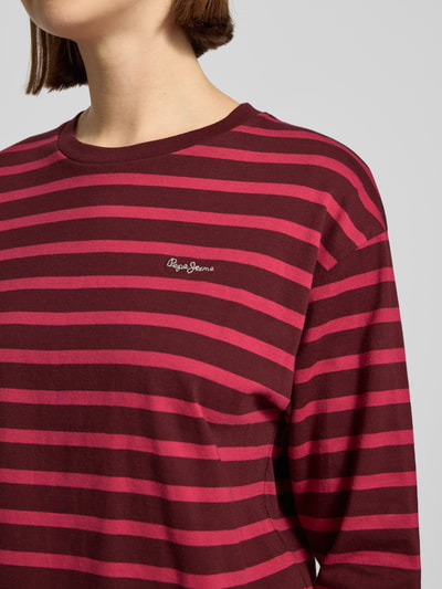Frauenmodel trägt Comfort Fit Langarmshirt aus reiner Baumwolle Modell 'BANILLA' von Pepe Jeans mit rot-pinkem Allover-Streifenmuster, Label Stitching und Rundhals, Nahaufnahme Oberkörper.