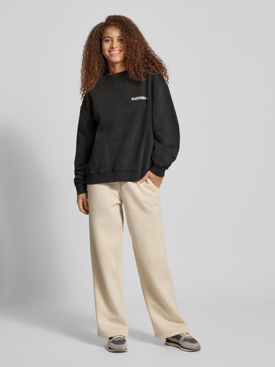 Frauenmodel trägt Oversized Sweatshirt mit Statement-Print von Karo Kauer, schwarz, aus reiner Baumwolle, weite Passform, Rundhalsausschnitt, gerippte Abschlüsse, Ganzkörperansicht von vorne.