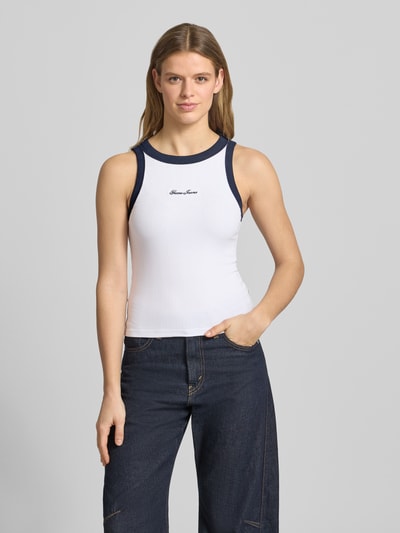 Vrouwenmodel draagt Tanktop in Ripp-Optik mit Label-Stitching van Guess Jeans in wit met donkerblauw, katoenmix met modal, slim fit, riblook, labelstitching op de borst, ruglengte bij maat S 50 cm, vooraanzicht bovenlichaam.