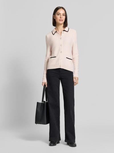 Frauenmodel trägt Regular Fit Cardigan aus Kaschmir-Mix von Christian Berg Woman in Hellrosa mit schwarzen Details, Umlegekragen, aufgesetzte Taschen, durchgängige Knopfleiste, schwarze Hose, neutrale Farbgebung, Textur weich und glatt, ganzkörperansicht von vorne.