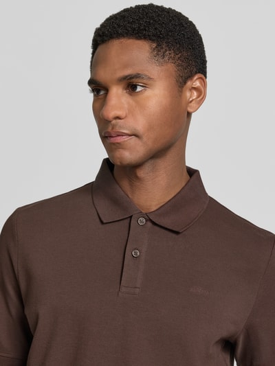 Męski model nosi Regular Fit Poloshirt aus reiner Baumwolle od s.Oliver RED LABEL, kolor brązowy, gładki, pikowana faktura, krótki rękaw, kołnierzyk polo, krótkie zapięcie na guziki, przód, zbliżenie na górną część ciała.