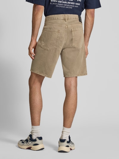 Männermodel trägt Regular Fit Jeansshorts aus reiner Baumwolle Modell 'EDGE' von Only & Sons in Denim-Optik mit Nieten, Label-Patch, 5-Pocket-Design; Farbe Beige, Materialstruktur glatt, Ganzkörperansicht Rückansicht.