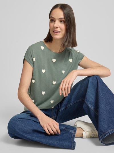 Frauenmodel trägt Relaxed Fit T-Shirt aus Lyocell-Mix Modell 'AVA' von Vero Moda, grünes Allover-Herz-Muster, Rundhals, Kurzarm, Ganzkörperansicht von vorne.