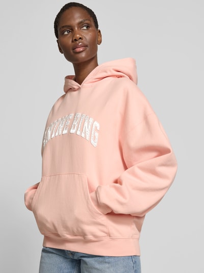Frauenmodel trägt Oversized Hoodie mit Logo-Detail von Anine Bing aus Reine Baumwolle in Rosa, Känguru-Tasche, elastische Abschlüsse, Oversized-Fit, Rückenlänge bei Größe S: 64 cm, Nahaufnahme Oberkörper.