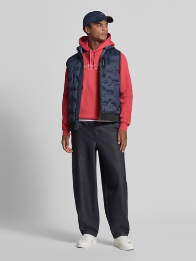 Mannenmodel draagt Relaxed Fit Hoodie uit katoenmix van Polo Ralph Lauren in rood, donkere spijkerbroek, Ganzkörperansicht von vorne.