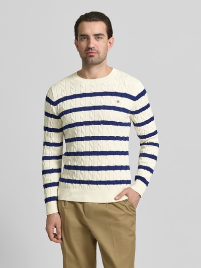 Männermodel trägt Slim Fit Pullover in Strick-Optik von Gant, creme mit blauen Streifen, Rundhals, Logo, Vorderansicht Oberkörper.