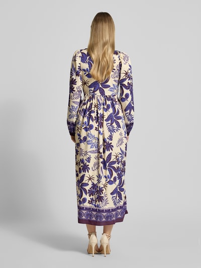 Frauenmodel trägt Midikleid aus Viskose-Mix Modell 'Sarai' von LOLLYS LAUNDRY mit Allover-Look, V-Ausschnitt, 3/4-Arm, Rückenlänge 122 cm, Brustweite 41 cm, Ärmellänge 56 cm, Muster in Creme und Violett, A-Linie, Ganzkörperansicht Rückansicht.