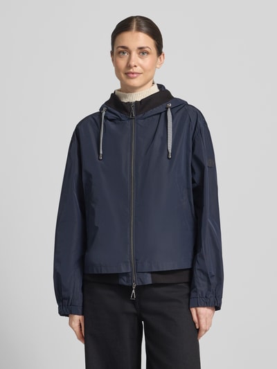 Modelka nosi Kurtka 'Jacke mit Zweiwege-Reißverschluss' od Gil Bret, krój relaxed fit, kaptur z tunelem, wpuszczane kieszenie, długość tyłu w rozmiarze 36: 59 cm, szerokość ramion: 52 cm, szerokość klatki piersiowej: 57 cm, długość rękawów: 57 cm, granatowy, lekko błyszcząca tekstura, całkowity widok z przodu.
