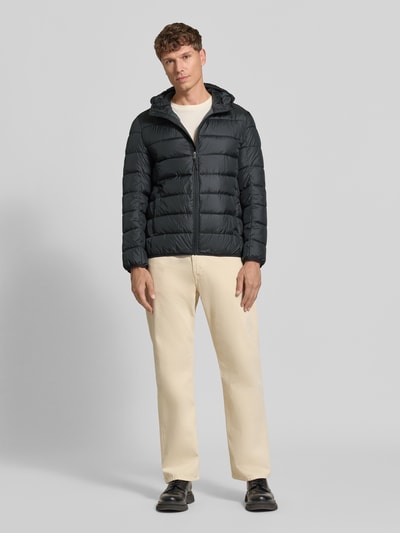 Męski model nosi Steppjacke mit Kapuze und Reißverschluss od MCNEAL w kolorze czarnym, proste pikowanie, krój regular fit, kaptur, zamek błyskawiczny, wpuszczane kieszenie, długość tyłu w rozmiarze M: 70 cm, szerokość ramion w rozmiarze M: 46 cm, szerokość klatki piersiowej w rozmiarze M: 54 cm, długość rękawów w rozmiarze M: 63 cm, widok całej sylwetki z przodu.