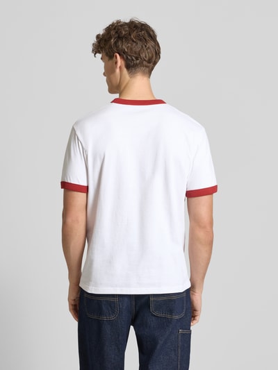 Männermodel trägt weißes T-Shirt im Retro-Look mit Label-Print von Carhartt Work In Progress, rote Bündchen, Baumwolle, Ganzkörperansicht Rückansicht.