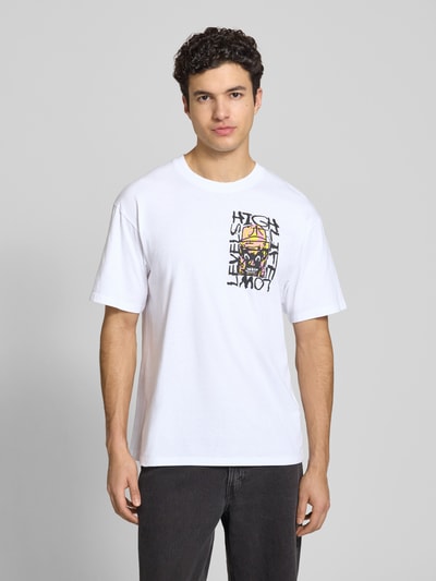Męski model nosi t-shirt z nadrukiem model 'HATTY MAN' od Edwin, czysta bawełna, krój relaxed fit, okrągły dekolt, długość tyłu w rozmiarze M: 73 cm, widok całej sylwetki z przodu.
