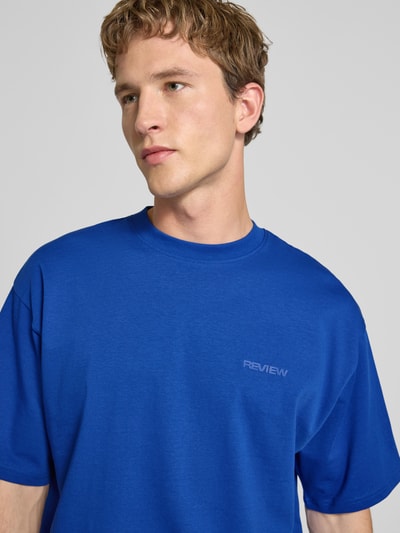 Männermodel trägt Oversized T-Shirt mit Logo von REVIEW in Blau, Reine Baumwolle, Rundhalsausschnitt, Nahaufnahme Oberkörper.