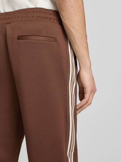 Männermodel trägt Regular Fit Sweatpants mit elastischem bund Modell 'RIBER' van Only & Sons, unie bruin met contrasterende streep, fijne weefstructuur, zijzakken, detailopname heup.