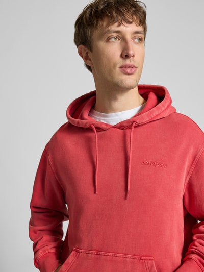 Männermodel trägt Hoodie mit Label-Stitching und Känguru-Tasche von Dickies in Rot, Relaxed Fit, Baumwoll-Mix, Nahaufnahme Oberkörper.