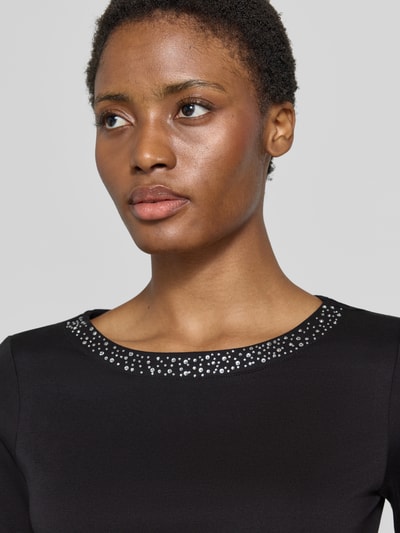 Frauenmodel trägt Regular Fit Shirt aus reiner Baumwolle von Christian Berg Woman in Schwarz mit Ziersteinen am U-Boot-Ausschnitt, Nahaufnahme Oberkörper.