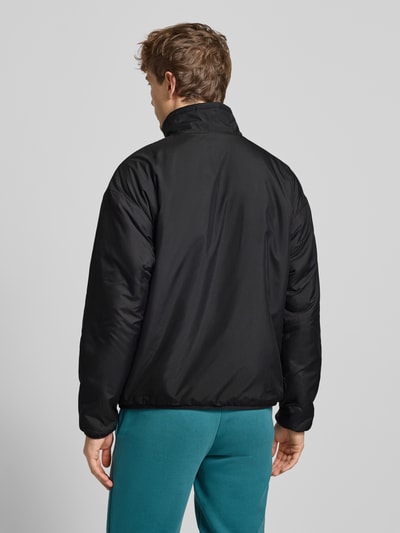 Mężczyzna nosi Sherpa Jacket mit Reißverschluss od PUMA PERFORMANCE, czarna, luźny krój, stójka, gładka tekstura, widok tyłu, Ganzkörperansicht Rückansicht. Długość tyłu 68 cm, szerokość ramion 60 cm, szerokość klatki piersiowej 63 cm, długość rękawów 59 cm, nadruk z logo, kieszenie zapinane na zamek błyskawiczny.