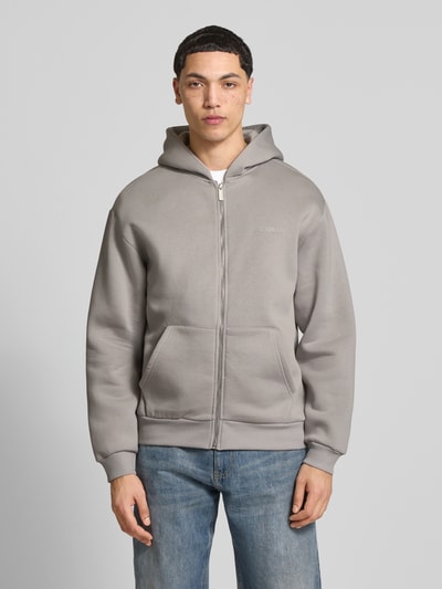 Męski model nosi Sweatjacke mit Känguru-Tasche od REVIEW, bawełniany mix, krój relaxed fit, szary, zamek, kieszeń kangurka, widok z przodu na całą sylwetkę