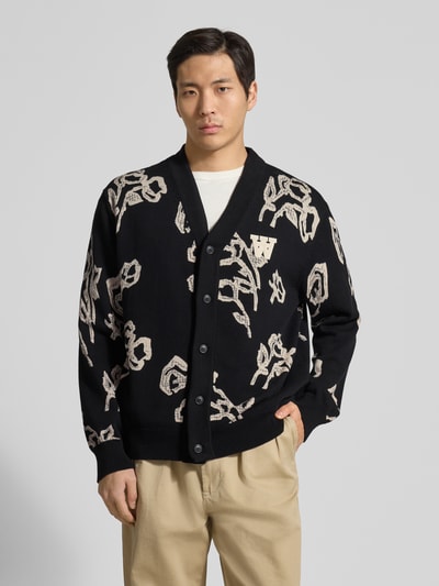 Męski model nosi Cardigan im Allover-Look Modell 'Leif' od Wood Wood, czarna bawełna organiczna, krój regular fit, dekolt w serek, zapięcie na guziki, widok całej sylwetki z przodu.