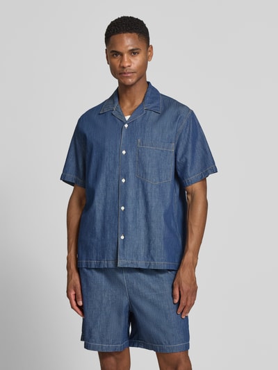 Männermodel trägt Relaxed Fit Freizeithemd aus reiner Baumwolle von Lacoste in Denim-Optik mit Resortkragen und Brusttasche, Ganzkörperansicht von vorne