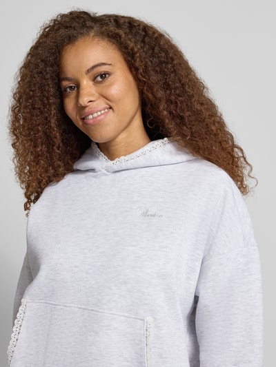 Frauenmodel trägt Relaxed Fit Hoodie mit Baumwoll-Anteil von REVIEW, hellgrau, Spitzenbesatz, Logo-Stitching, Känguru-Tasche, Nahaufnahme Oberkörper.