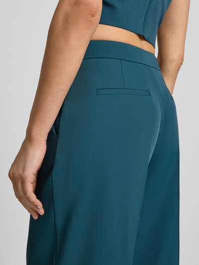 Vrouwenmodel draagt Hose mit weitem Bein und Paspeltaschen am Gesäß van Jake*s Cocktail in blauwgroene kleur, materiaal-mix met stretch, paspelzakken achter, biesplooien, detailopname billen.