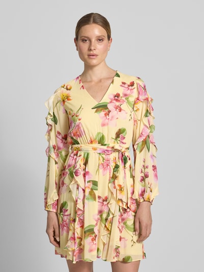 Frauenmodel trägt Knielanges Cocktailkleid mit Chiffons und Bindegürtel von V by Vera Mont, gelber Allover-Look mit Volants, V-Ausschnitt, Taillierter Schnitt, florales Muster, weiche Textur, Nahaufnahme Oberkörper.