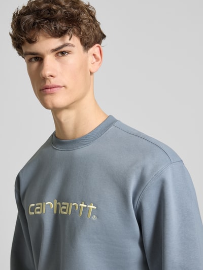 Männermodel trägt Sweatshirt mit Label-Stitching von Carhartt Work In Progress in Blau, Baumwoll-Mix, lockere Passform, Nahaufnahme Oberkörper.