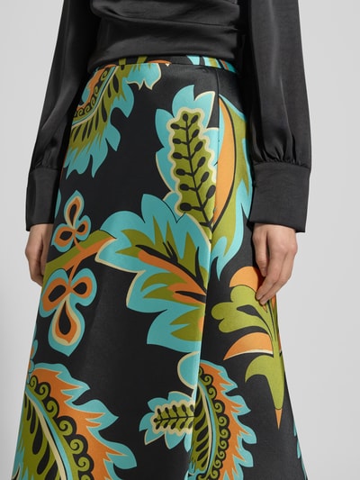 Frauenmodel trägt Midirock aus Satin im Allover-Look von HERZENS, schwarze Grundfarbe, bunte Blätter, Teilungsnähte, Nahaufnahme Oberkörper.