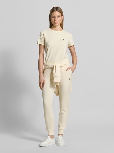 Modelka nosi Regular Fit T-Shirt mit Logo-Applikation Modell 'Colette' von Guess Activewear z elastycznej mieszanki bawełny, krój regular fit, okrągły dekolt, długość tyłu w rozmiarze S: 60 cm, jasny kremowy kolor, gładka struktura, widok całej sylwetki z przodu.