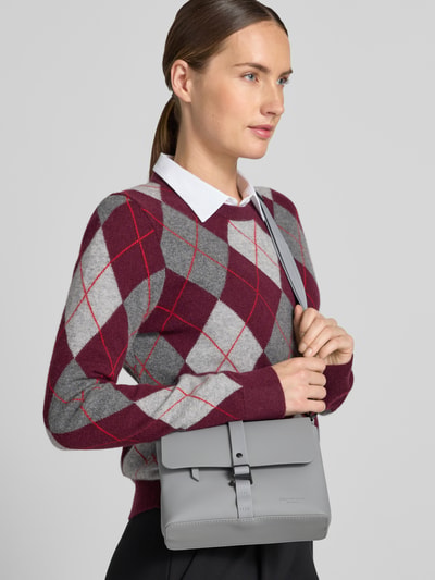 Frauenmodel trägt Umhängetasche mit Logo-Prägung Modell 'SPLÄSH' von GASTON LUGA in Hellgrau, schlichtes Design, Nahaufnahme Oberkörper. Hauptfach mit Umschlag, verstellbarer Schultergurt, Reißverschlussfächer, strukturierte Oberfläche.