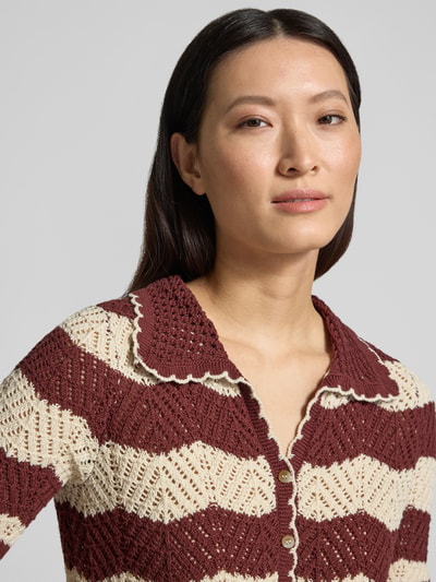 Kobiece modelka nosi Regular Fit Cardigan aus reiner Baumwolle Modell 'GOLDEN COVE' von Vero Moda, imitacja dzianiny, wzór w paski, krój regular fit, listwa guzikowa, dekolt w serek, krótki rękaw, wykończenie: dzianina, materiał: bawełna, kolor bordowy i kremowy, zbliżenie na górną część ciała.