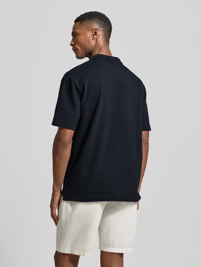 Männermodel trägt Relaxed Fit Poloshirt aus reiner Baumwolle von Marc O'Polo in Schwarz mit Webstruktur, unifarben, Rückansicht Ganzkörperansicht.