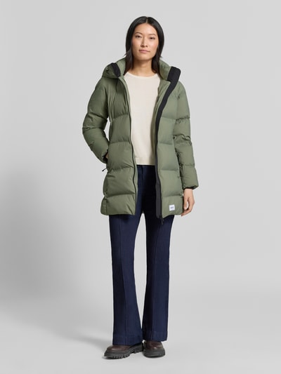 Modelka nosi Regular Fit płaszcz w z efektem pikowania z naszywką z logo model 'TANARE' od khujo w kolorze oliwkowym, zamek błyskawiczny dwustronny, Długość tyłu w rozmiarze S: 82 cm, Szerokość ramion w rozmiarze S: 47 cm, Szerokość klatki piersiowej w rozmiarze S: 47 cm, Długość rękawów w rozmiarze S: 59 cm, widok całej sylwetki z przodu.