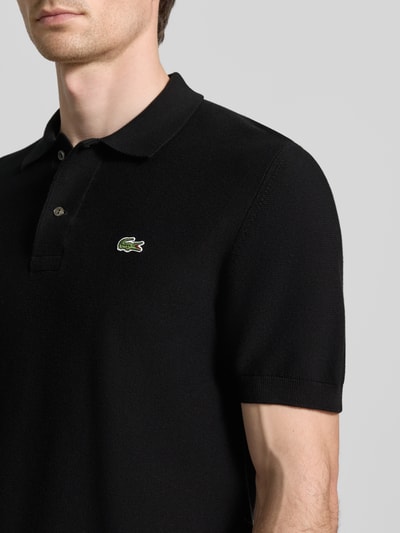 Mężczyzna model ma na sobie Regular Fit Poloshirt aus reiner Baumwolle od Lacoste, czarny, gładki, logo, krój regular fit, bawełna. Nahaufnahme górnej części ciała.