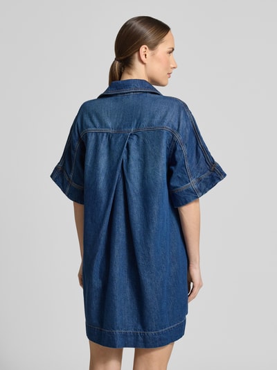 Frauenmodel trägt Regular-Fit Jeanskleid aus Baumwoll-Mix mit Lyocell-Anteil von BOSS Orange in Denim-Optik, Kurzarm, Mini-Länge, Rückenpasse mit Kellerfalte, Brusttasche, Materialverarbeitung Twill, Ganzkörperansicht Rückansicht.