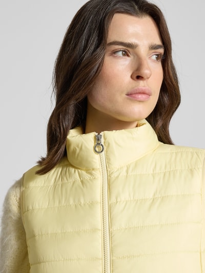 Frauenmodel trägt Regular Fit Steppweste mit Reißverschlusstaschen von s.Oliver RED LABEL in unifarbenem Gelb, Stehkragen, Nahaufnahme Oberkörper.