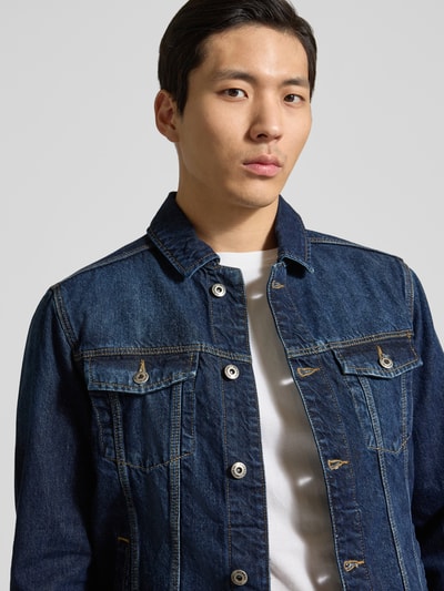 Męski model nosi Jeansjacke mit Brusttaschen von MCNEAL, niebieski dżins, krój regular fit, bawełna, z przodu kieszenie, kołnierz, zapięcie na guziki, szerokość w rozmiarze M: 48 cm, długość tyłu: 62 cm, szerokość klatki: 27 cm, długość rękawa: 64 cm, półzbliżenie górnej części ciała z przodu.