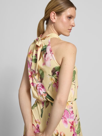 Modelka nosi Regular Fit Jumpsuit mit floralem Allover-Print von V by Vera Mont, żółte tło z kwiatowym wzorem, cut-out z tyłu, detal wiązania, bez rękawów, Szerokość w rozmiarze 36: 36 cm, długość tyłu: 147 cm, długość całkowita: 132 cm, długość nogawki: 81 cm, tkanina o gładkiej fakturze, zamek w szwie, widok z tyłu, zbliżenie na górną część pleców.