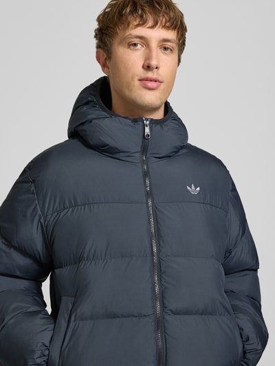 Männermodel trägt Regular Fit Puffer Jacket mit Kapuze von adidas Originals in Dunkelblau, unifarben, mit Logo, Nahaufnahme Oberkörper.