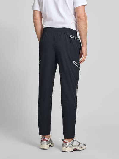 Männermodel trägt Regular Fit Sweatpants mit Logo-Print Modell 'Unstoppable' von Under Armour in Schwarz, Elastischer-Material-Mix, Cargo-Taschen mit Reißverschluss, Elastischer Bund, Innenbeinlänge bei Größe M 79 cm, Ganzkörperansicht Rückansicht.