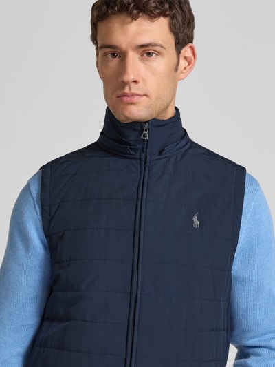 Männermodel trägt Steppweste mit Kapuze und Label-Stitching von Polo Ralph Lauren in Dunkelblau, Regular Fit, Nahaufnahme Oberkörper. Rückenlänge 31 cm, Schulterbreite 42 cm, Brustweite 58 cm, Stehkragen, Reißverschluss.