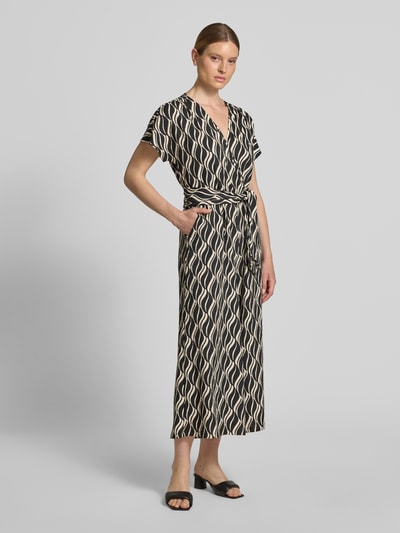 Frauenmodel trägt Jumpsuit im Allover-Look mit V-Ausschnitt von Betty Barclay, Muster in Schwarz und Beige, Taillenband, Ganzkörperansicht von vorne. Material-Mix mit Stretch-Anteil und Regular Fit, Rückenlänge 42 cm, Brustweite 40 cm, Ärmellänge 34 cm, Gesamtlänge 136 cm, Innenbeinlänge 64 cm bei Größe 36.